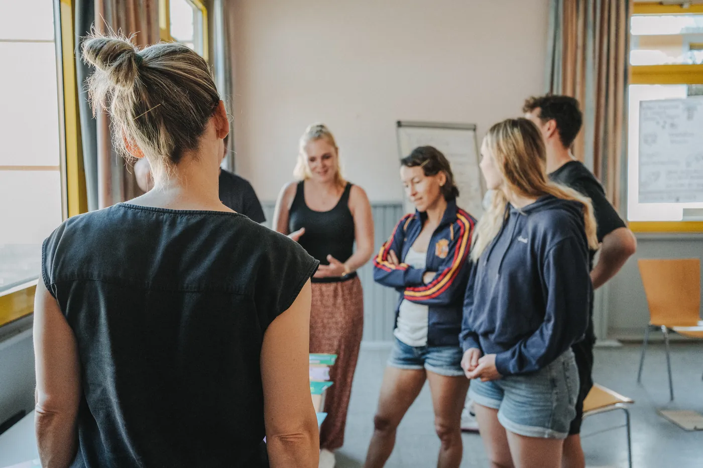 Teilnehmende eines Workshops stehen im Halbkreis in einem Seminarraum, eine Frau erzählt, die anderen hören zu