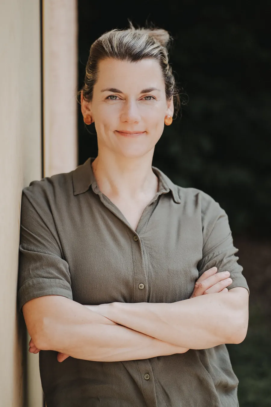 Porträt von Judith Rachel: lächelnd, die Arme verschränkt, grünes Hemd