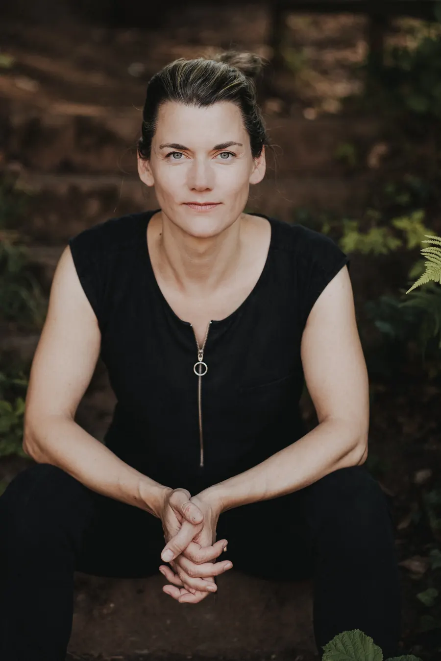 Judith Rachel sitzt auf einer Stufe im Grünen und schaut direkt in die Kamera