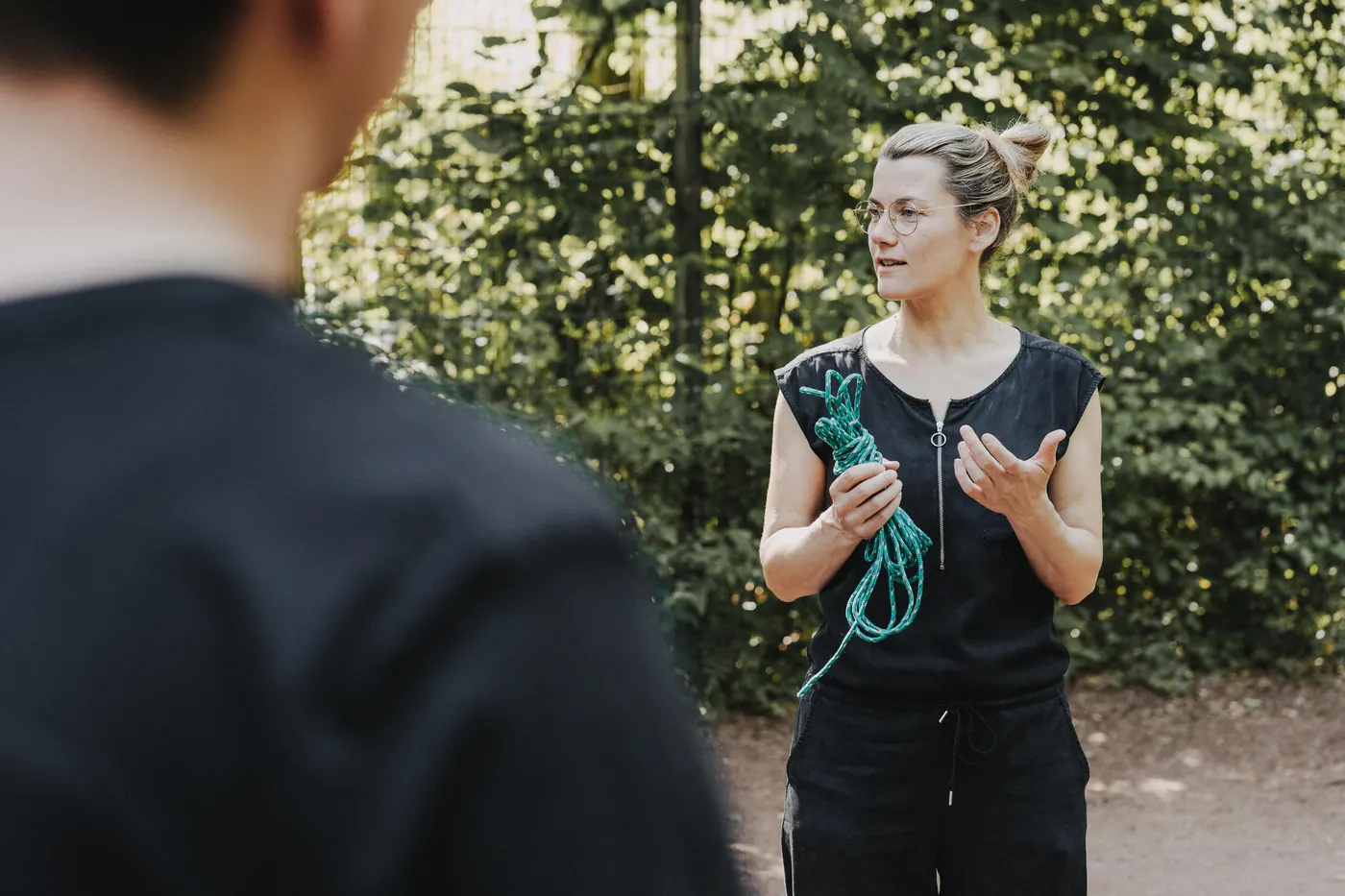 Judith Rachel erklärt einer Gruppe im Freien etwas, in der Hand ein grünes Seil